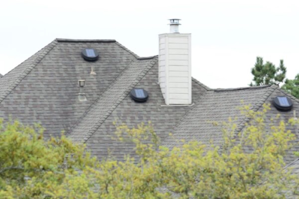 Two solar attic fans installed on a shingle roof near a chimney, providing powered exhaust ventilation
