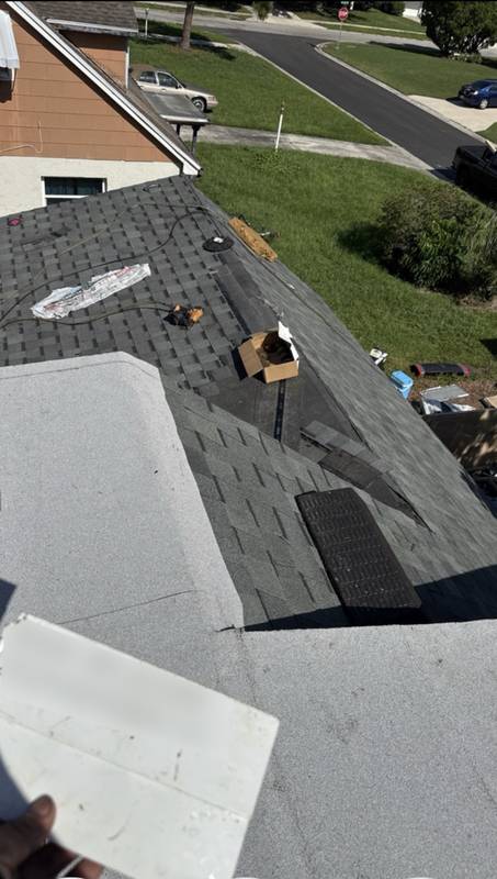 Dark gray shingles being installed on a roof with tools and materials laid out