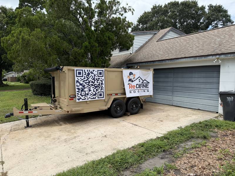 Redefine Roofing equipment trailer with QR code and logo banner at a job site