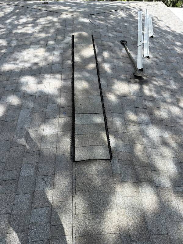 Gray shingle roof with a black strip and tools laid out during installation
